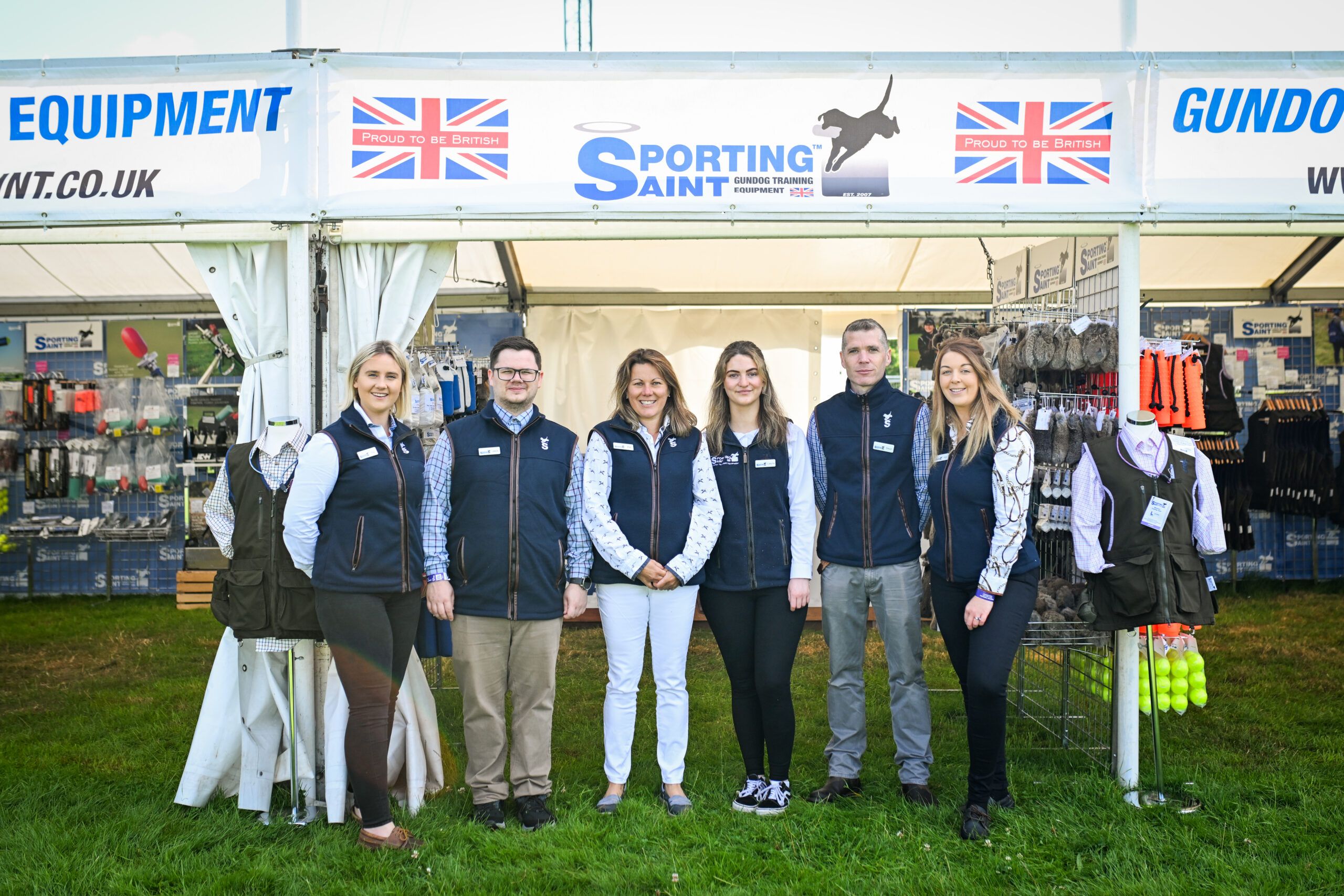 The Sporting Saint team stand in a line in front of their stand at The Game Fair